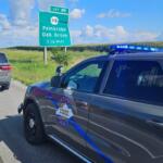 Two Kentucky State Police SUVs with blue lights parked on a rural highway next to an exit sign for Pembroke and Oak Grove, 1½ miles away.