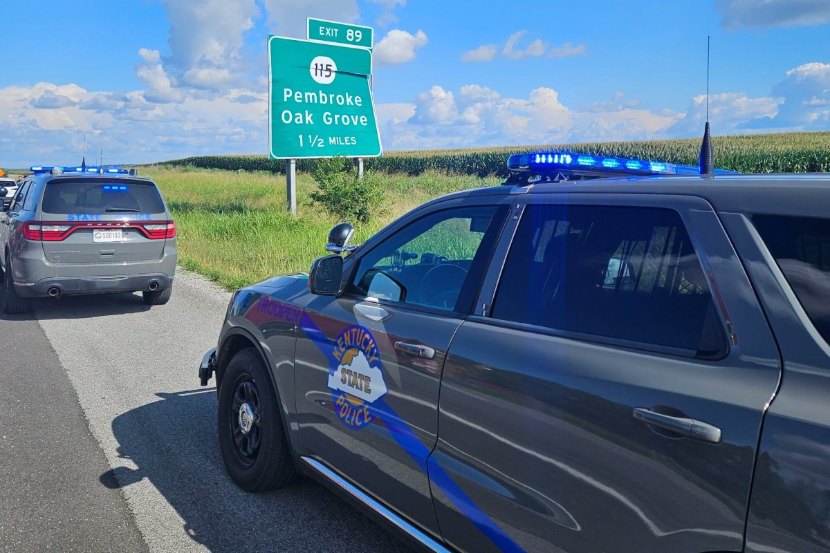 Two Kentucky State Police SUVs with blue lights parked on a rural highway next to an exit sign for Pembroke and Oak Grove, 1½ miles away.