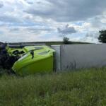 Lime-green sports car overturned on its roof against a gray trailer on a grassy roadside, engine exposed after a crash.