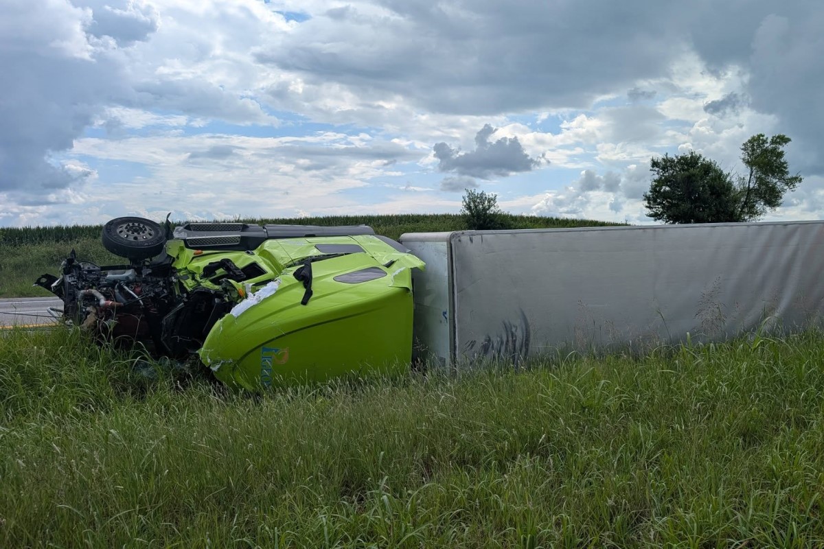 Lime-green sports car overturned on its roof against a gray trailer on a grassy roadside, engine exposed after a crash.