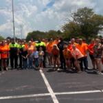Large group of people in orange shirts posing together in a parking lot on a sunny day.