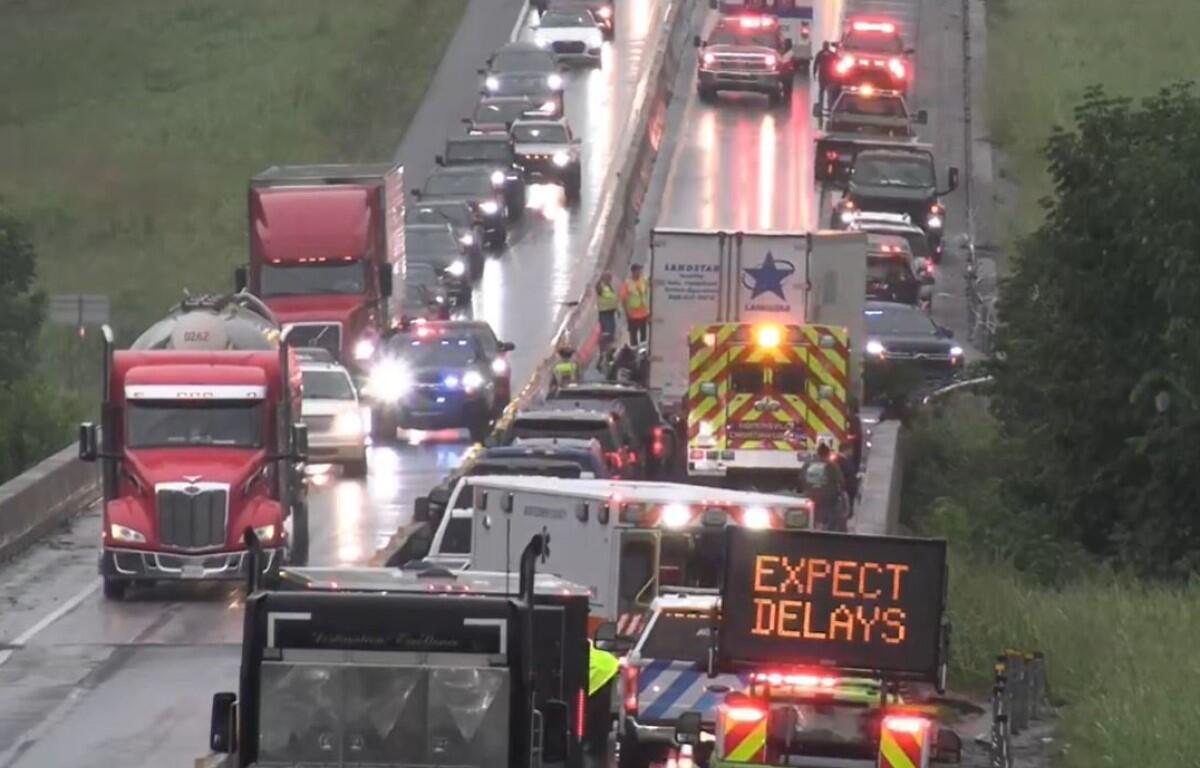 Highway scene with emergency vehicles and a bright sign that reads 'EXPECT DELAYS' amid a traffic backup on a wet road