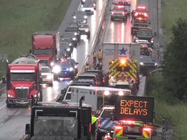 Highway scene with emergency vehicles and a bright sign that reads 'EXPECT DELAYS' amid a traffic backup on a wet road