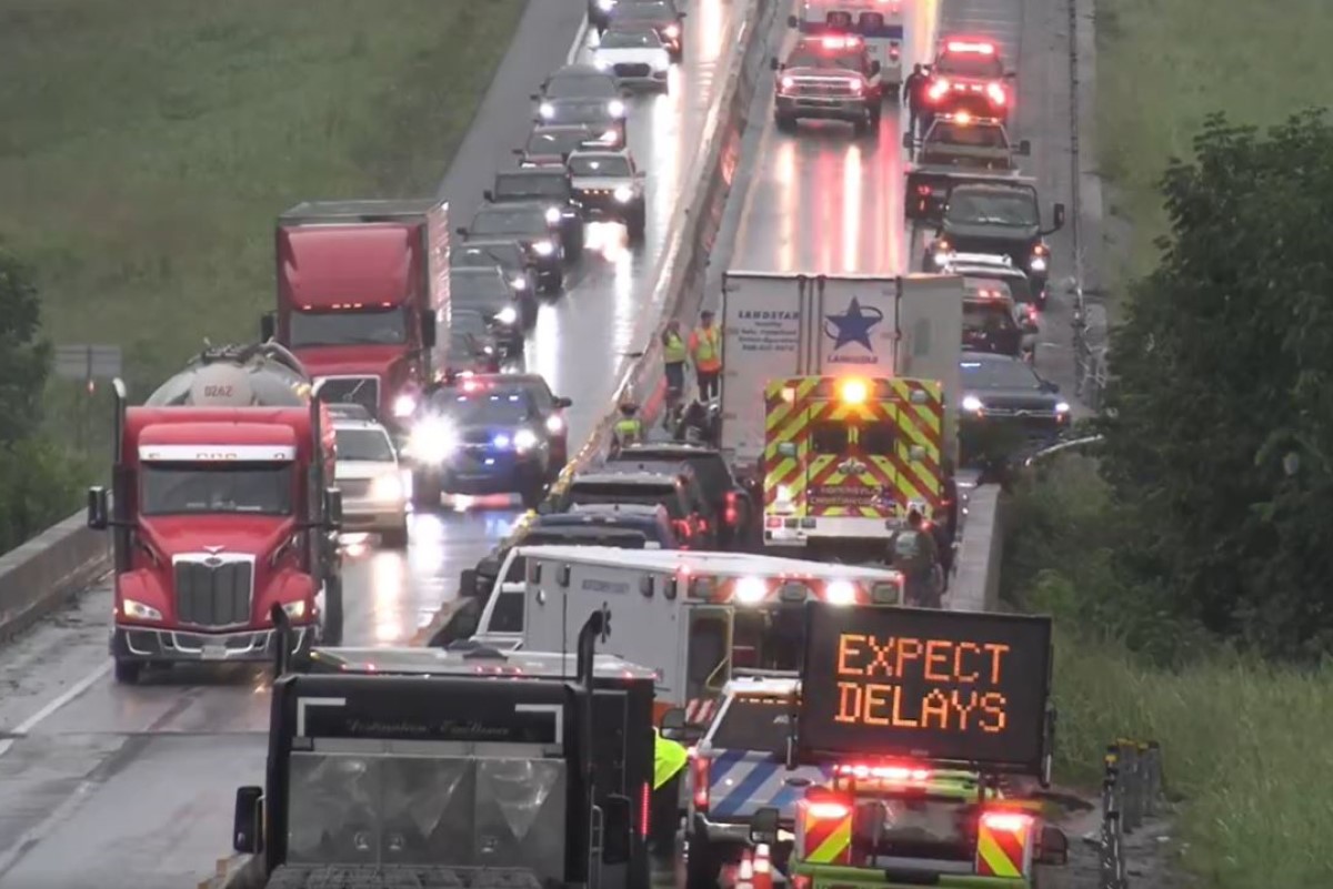 Highway scene with emergency vehicles and a bright sign that reads 'EXPECT DELAYS' amid a traffic backup on a wet road