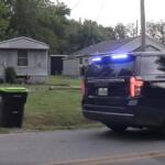 Sheriff SUV with blue lights on a residential street near mobile homes and a green trash bin in the yard.