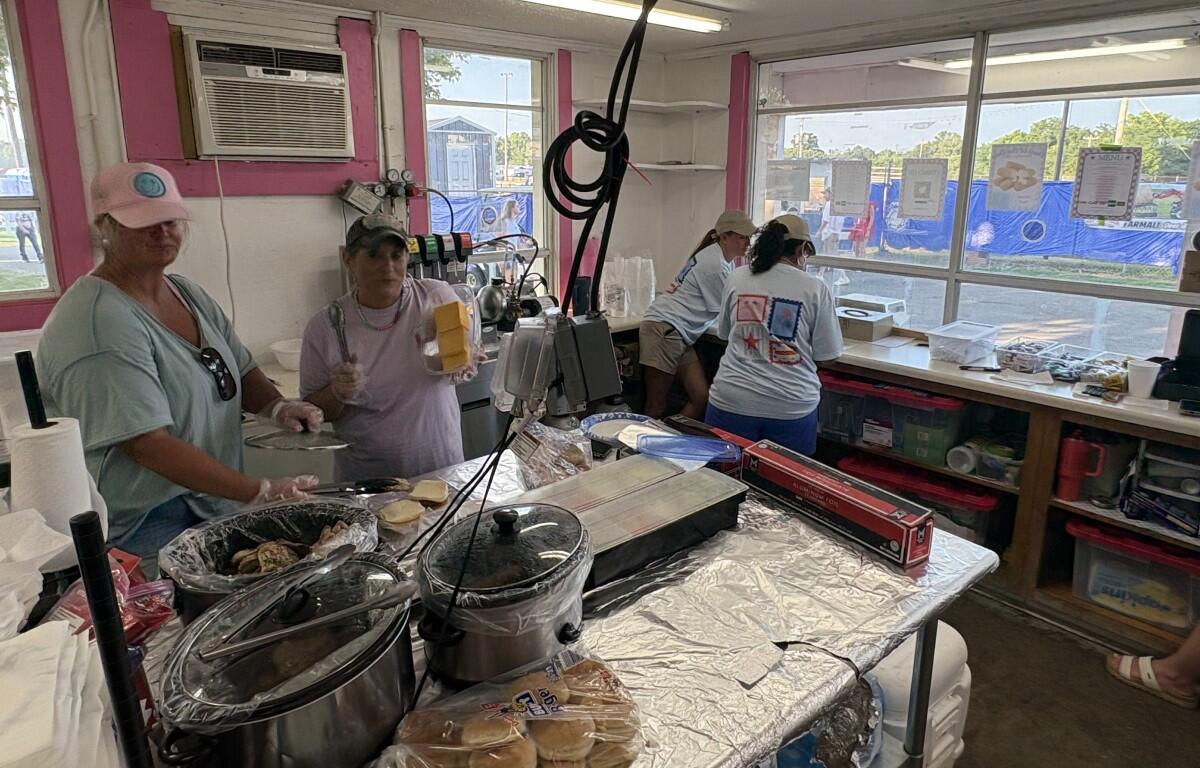 Concession booth with volunteers cooking and assembling food on foil-covered counter inside a pink-walled tent.