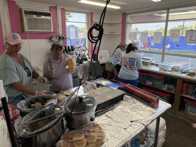 Concession booth with volunteers cooking and assembling food on foil-covered counter inside a pink-walled tent.