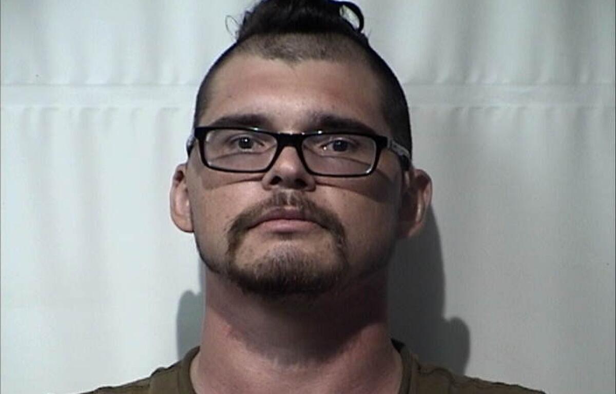 Mugshot of a man with short dark hair, glasses, and a goatee, facing the camera against a plain backdrop.