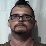 Mugshot of a man with short dark hair, glasses, and a goatee, facing the camera against a plain backdrop.