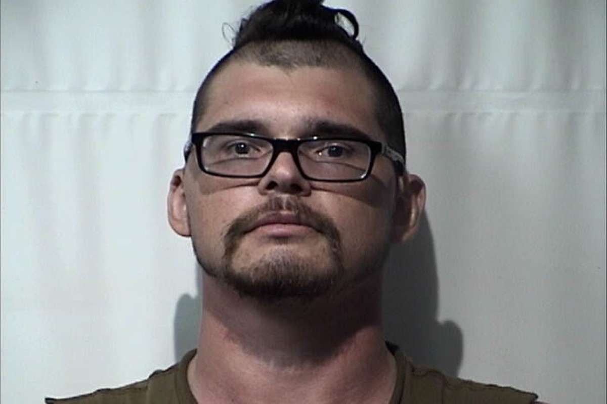Mugshot of a man with short dark hair, glasses, and a goatee, facing the camera against a plain backdrop.