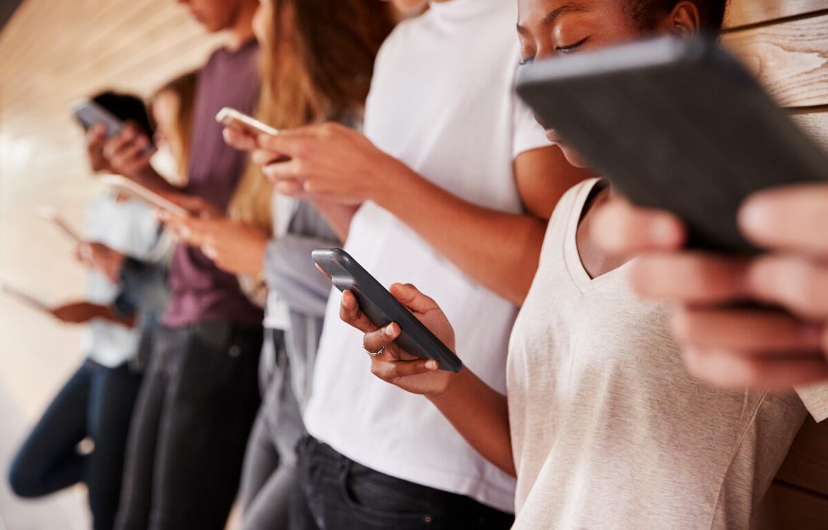 Group of young people leaning against a wall, each focused on their smartphones in a hallway wall-tiled setting.