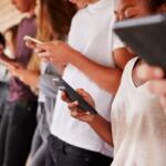 Group of young people leaning against a wall, each focused on their smartphones in a hallway wall-tiled setting.