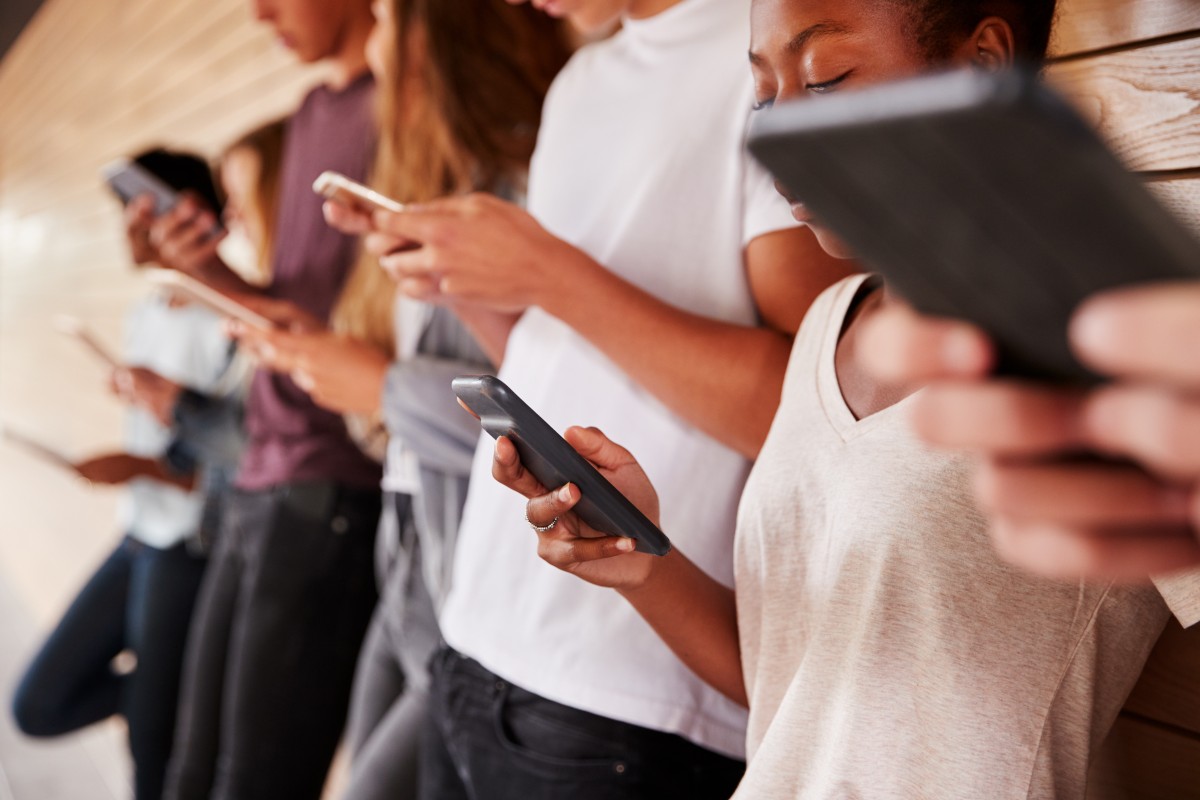 Group of young people leaning against a wall, each focused on their smartphones in a hallway wall-tiled setting.